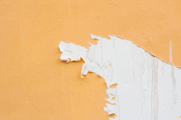 Крупный план облупившейся белой краски на оранжевой стене.